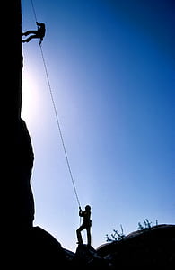 man climbing using rope near man on the ground looking up
