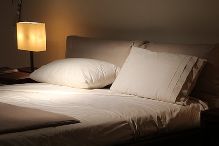 empty bed with white comforter set beside turned on table lamp