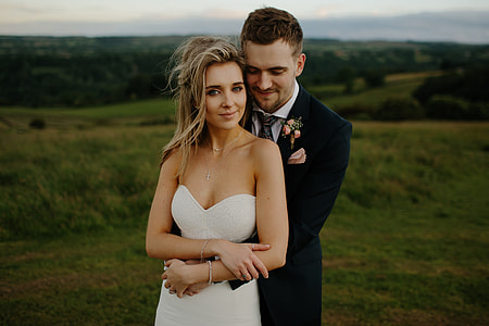 photo of woman in sweetheart neckline dress with man in black suit jacket, black necktie, and white dress shirt with green grass in the background