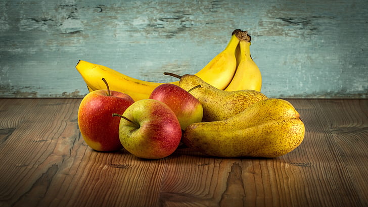 two bananas and three ripe apples on top of brown wooden surface