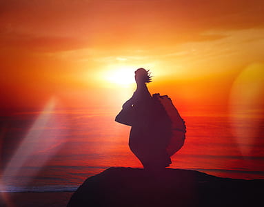 silhouette of person standing on cliff during sunset