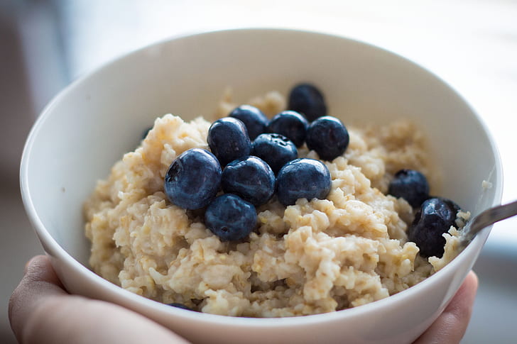 person holding bowl of oats with blue berries