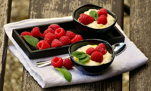 Raspberries on Black Rectangular Tray Beside Black Round Bowl With 3 Raspberries Beside Silver Spoon on Top of White Textile