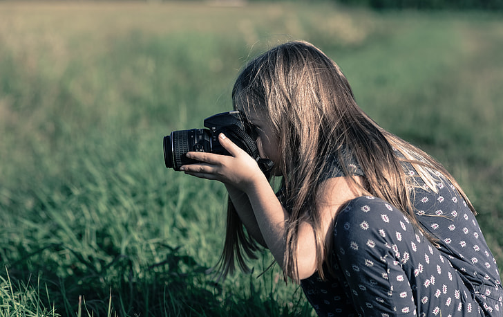 girl using black DSLR camera sitting on green grass field
