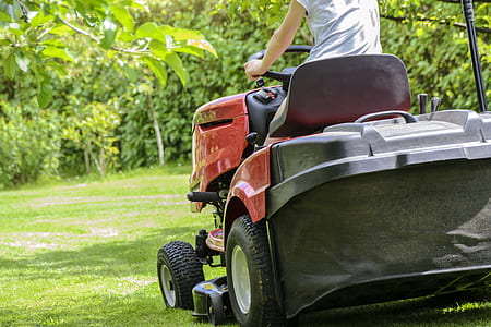 person riding red riding mower during daytime