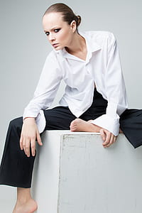close up photograph of woman in white dress shirt and black pants sitting on cube box