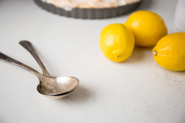 two stainless steel spoon beside lemons on top of table