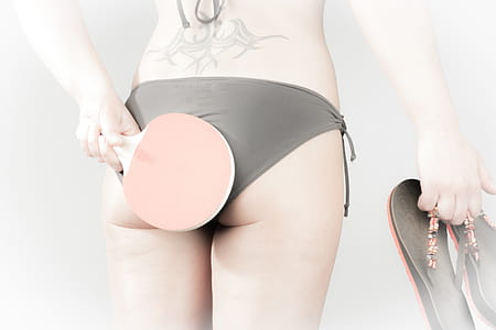 woman wearing black bikini bottoms holds ping pong paddle and flip-flops