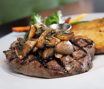 brown steak with mushroom toppings on white ceramic plate