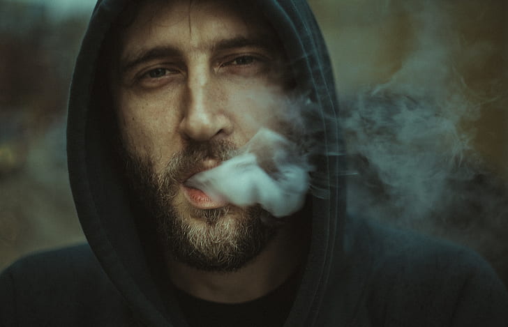 man in black hoodie releasing smoke through mouth