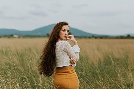 woman wearing white sheer long-sleeved crop top and yellow bodycon skirt standing in middle of grass field