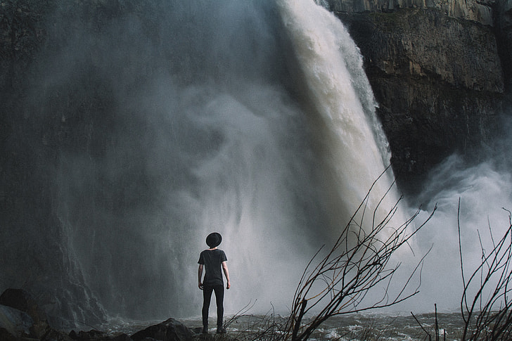 boy standing near waterfalls