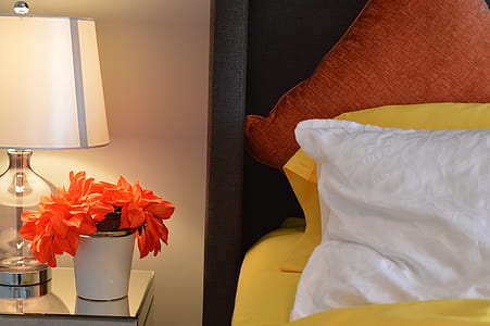 orange petaled flowers with white ceramic pot near bed with white pillow
