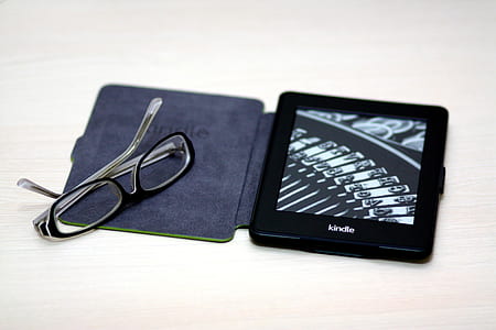 black Amazon Kindle e-book reader on brown surface near black framed eyeglasses