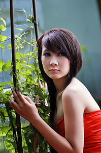 woman wearing red strapless top touching brown stick with green leaves at daytime
