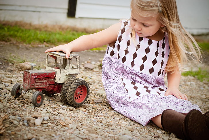 girl in white and purple sleeveless dress playing red and white toy car at daytime