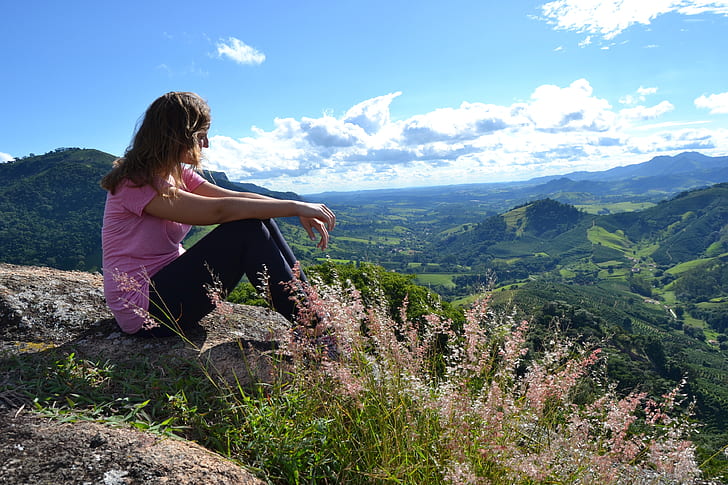 woman wearing pink t-shirt sitting above the mountain