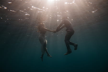 man and woman holding hand while floating on water