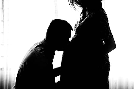 silhouette photo of man kissing belly of woman