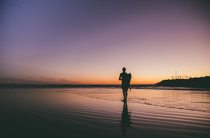 silhouette photo of man standing seashore during golden hour