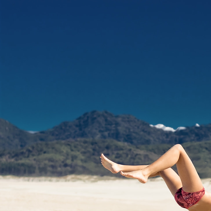 person with pink and black underwear flipping on white sand under blue sky