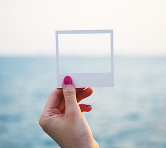 person's hand holding white square paper frame