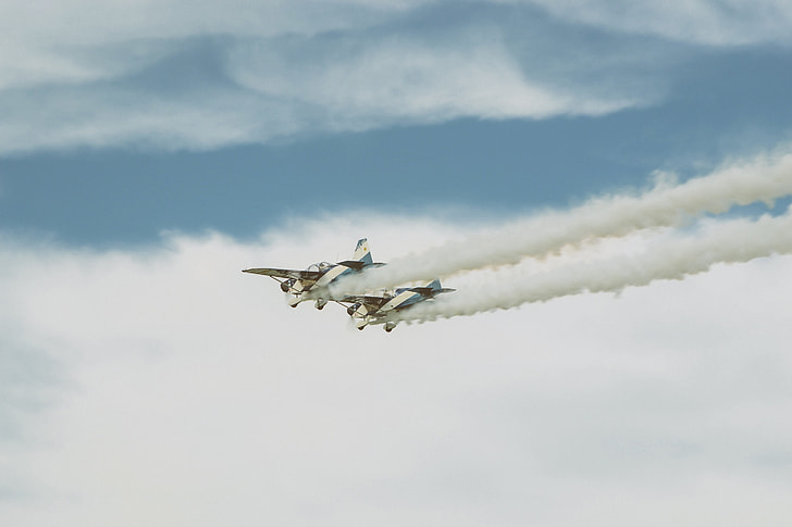 two white dog fighter planes throwing smoke on air under white cloudy skies