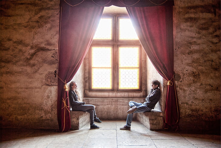 photo of man and woman sitting on terrace beside a window