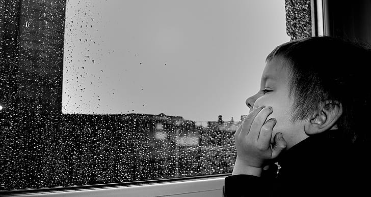 grayscale photography of boy watching the rain on window