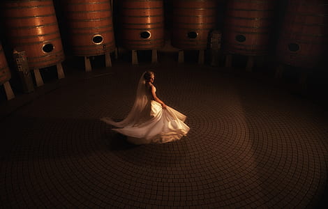 photography of woman in white wedding gown standing near brown wooden tank