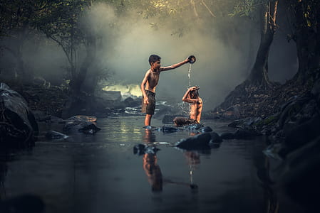 boy pouring water on person while on the river