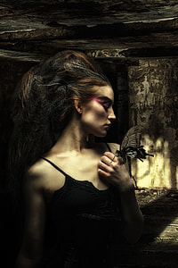 black and brown haired woman in black spaghetti strap top posing in abandon building with moth in her hand