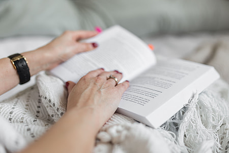 Soft photo of woman on the bed with the book and cup of coffee in hands