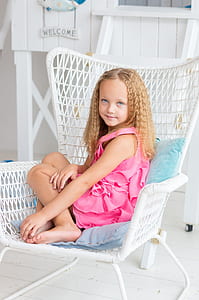 girl in pink sleeveless dress sitting on white wicker armchair