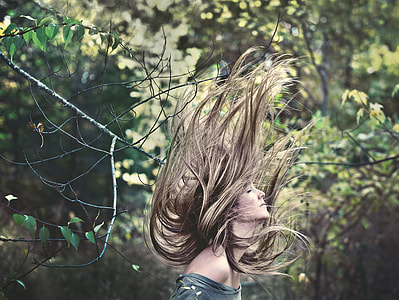 woman with blonde long hair flipping her hair near trees