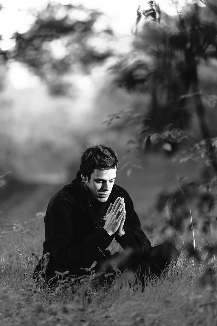 grayscale photograph of man sitting on grass