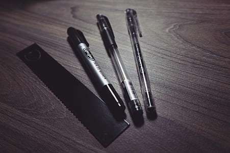 Three Ballpoint Pens and Black Ruler on Beige Wooden Surface