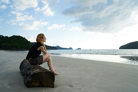 woman wearing black shirt with gray short sitting on brown slab near the body of water during daytime