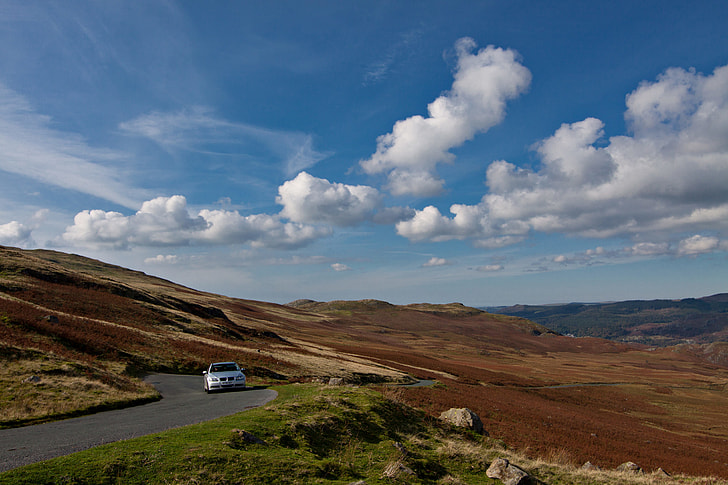 A BMW car drives along an open and twisting road in the Lake District in Cumbria, England