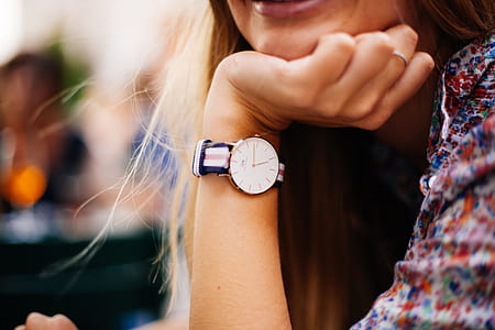 woman wearing round gold-colored analog watch with white-red-and-blue striped strap