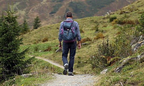 man in blue long-sleeved top and black pants with backpack walking during daytime
