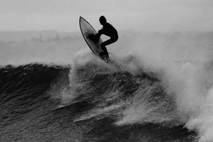 grayscale photo of man riding surfboard