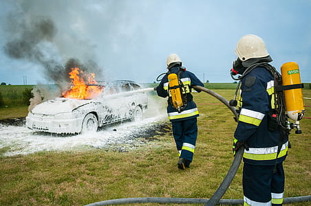 two firefighters fighting fire on grey station wagon on field during daytime