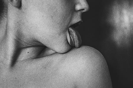 grayscale photography of person licking his/her shoulder