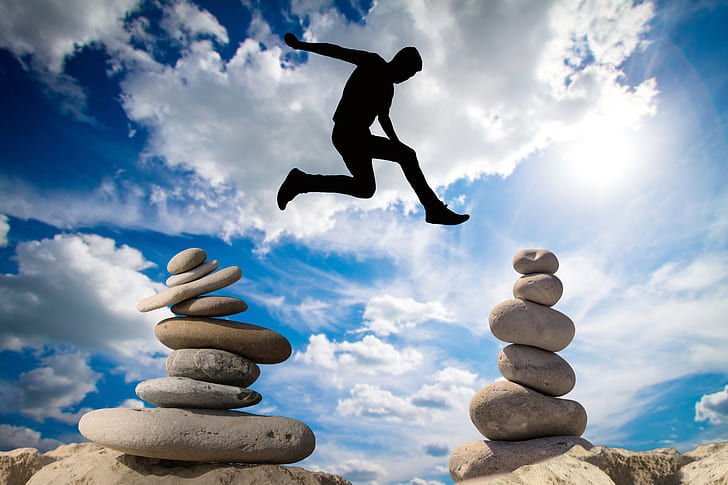 man jumping above balance stones