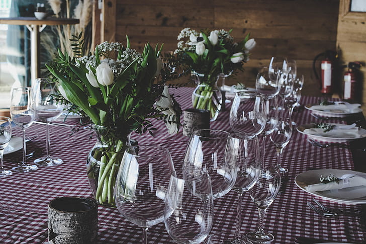 closeup photo of long-stem wine glasses near ceramic plates and white petaled flowers on talbe