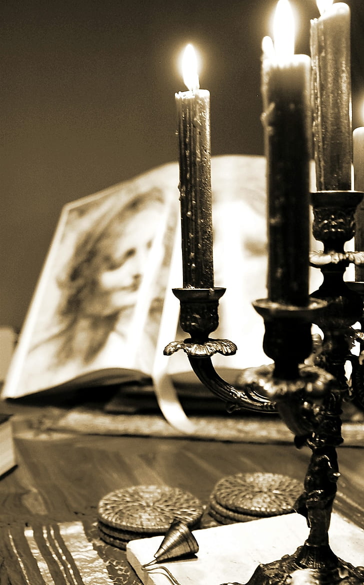 sepia photography of lighted candles with candelabra near open books