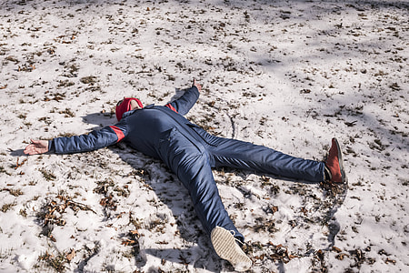 person in blue overalls lying on snow during daytime