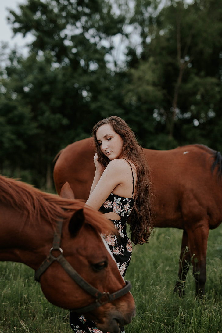 woman standing between two brown horses on green grass field