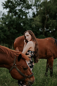woman standing between two brown horses on green grass field